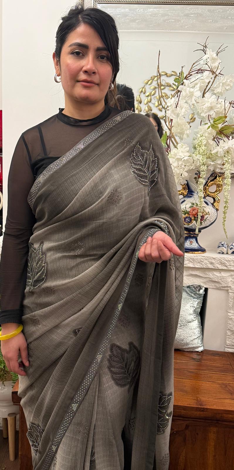 A mud grey chiffon saree adorned with delicate stone work,intricately arranged in graceful leafy ,motifs,lending it a refined and sophisticated charm.£55