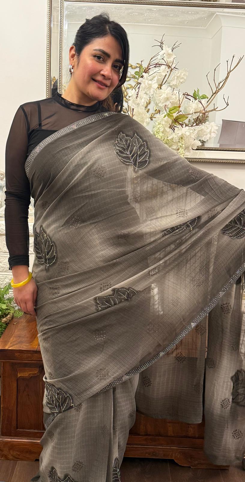 A mud grey chiffon saree adorned with delicate stone work,intricately arranged in graceful leafy ,motifs,lending it a refined and sophisticated charm.£55