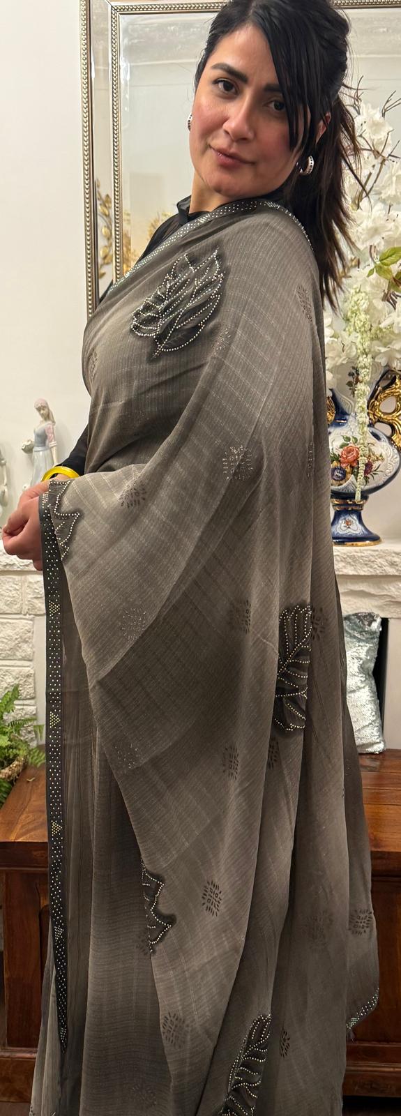 A mud grey chiffon saree adorned with delicate stone work,intricately arranged in graceful leafy ,motifs,lending it a refined and sophisticated charm.£55